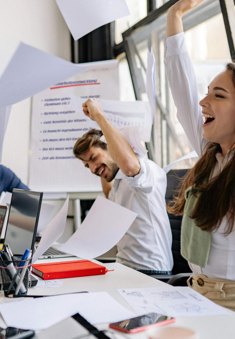 Die Trainingsteilnehmer, die am Tisch sitzen, freuen sich und werfen Papiere in die Luft.