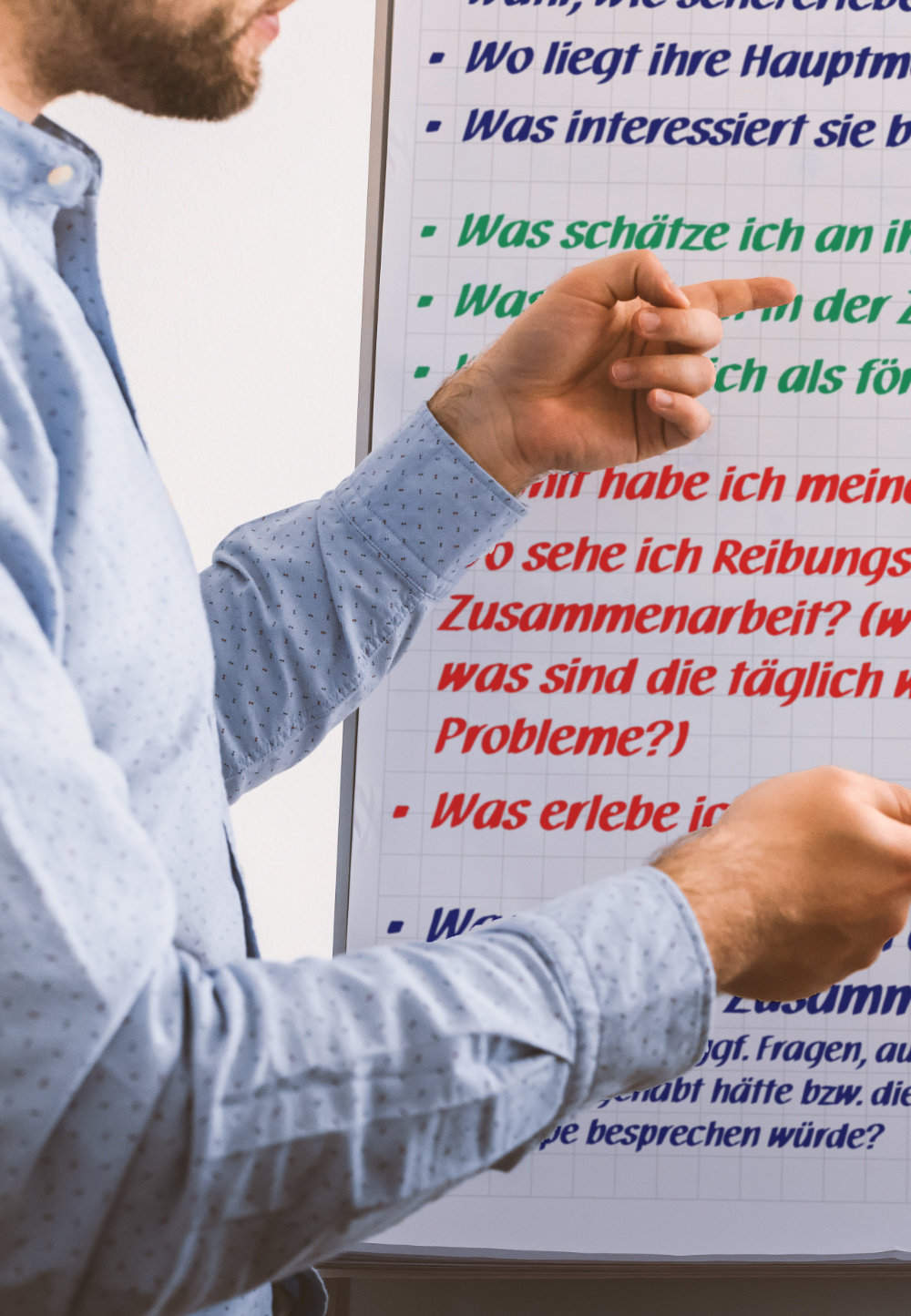 Ein Trainer zeigt mit den Händen auf die Texte eines Flipcharts.
